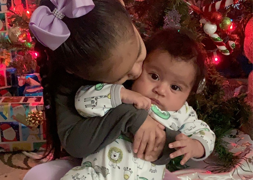 Jonathan's big sister gives him a sweet kiss in front of the Christmas tree.