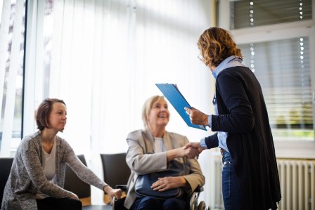 Shot of a physician shaking hands with senior woman sitting on wheelchair in hospital. Friendly medical doctor greeting senior patient.