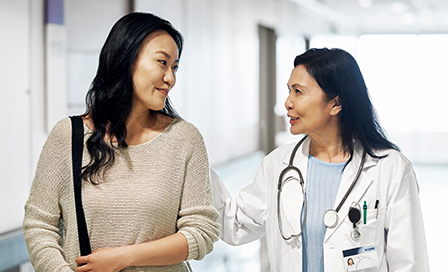 Smiling mature doctor talking to woman in hospital. Female patient visiting healthcare worker for routine checkup. They are standing in corridor.