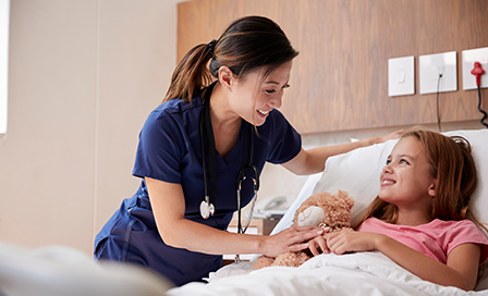 Female doctor treating a female child, who is lying in a hospital bed. 