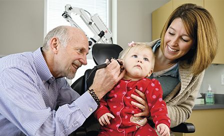 Doctor examining the ear of an infant with mother in the background