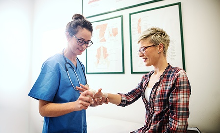 Female doctor checking a female patient's hands.