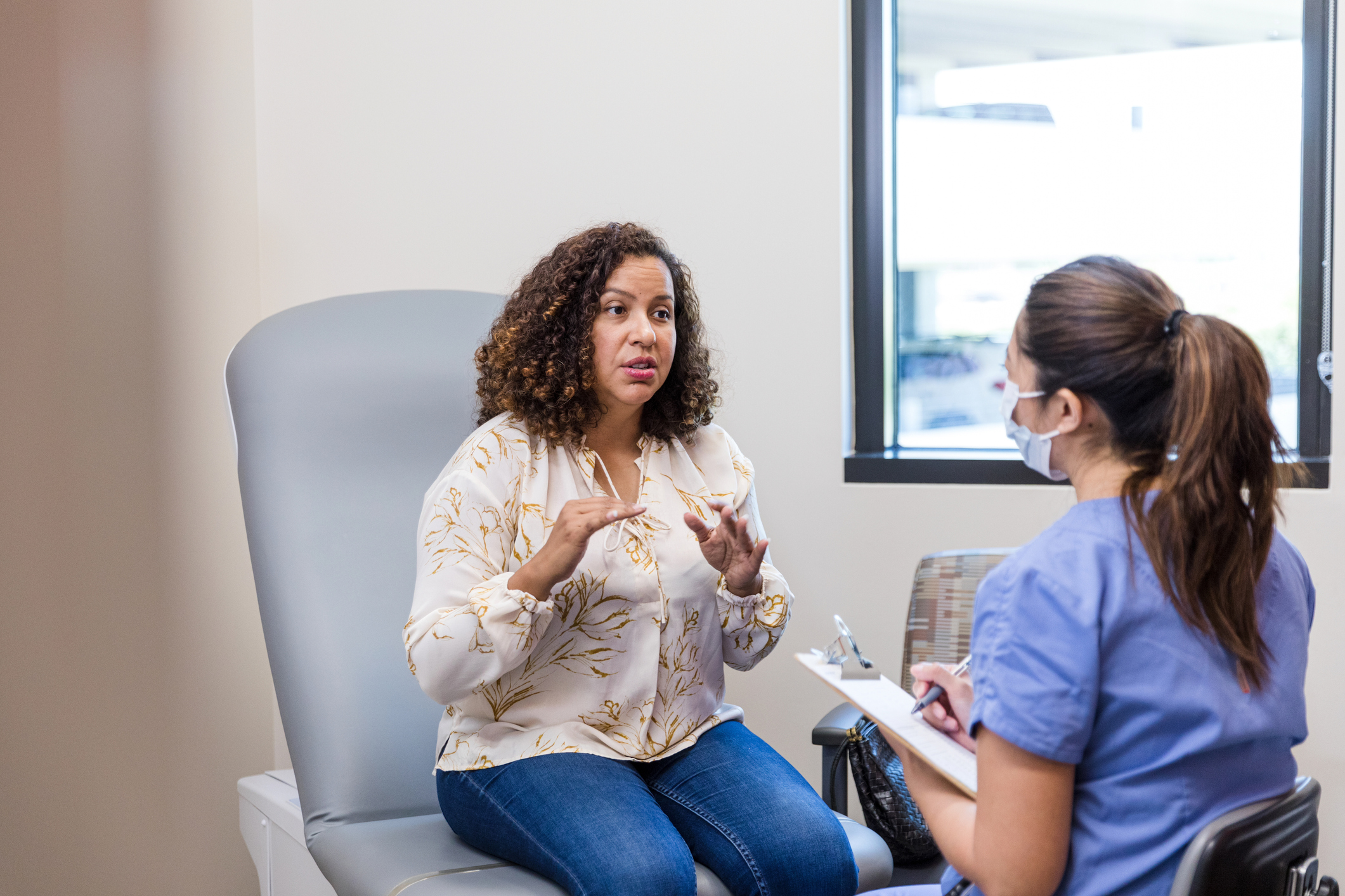 The female adult patient talks to the nurse about symptoms she has been experiencing.