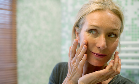 Mature woman looking at reflection in mirror with hand on cheek