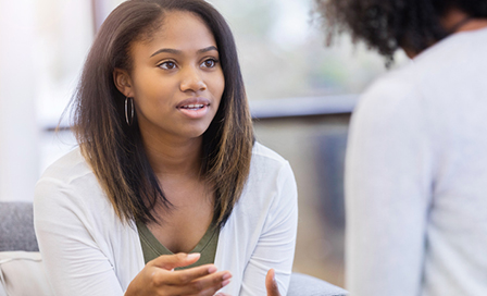 In this closeup, a young woman sits on a couch and leans forward as she talks to an unrecognizable therapist about her situation.