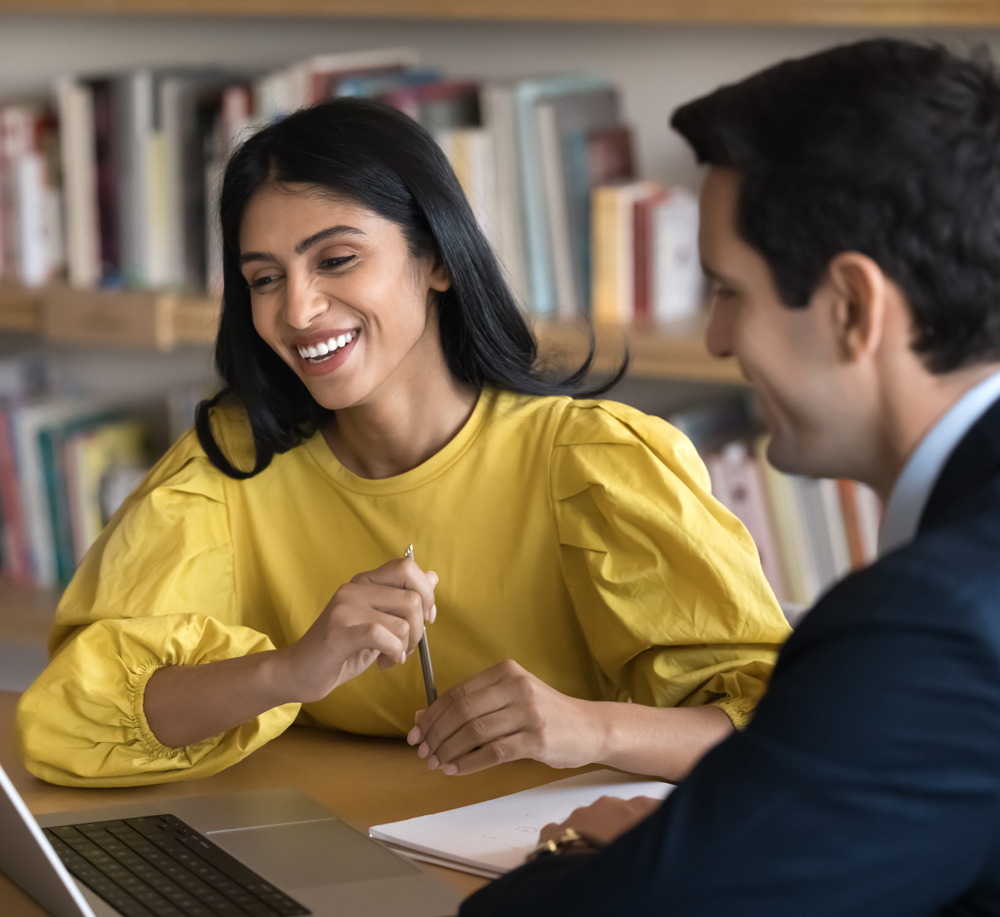 Women in yellow sitting with a man in a suit looking at a laptop. 