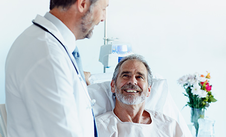 Happy mature patient looking at male doctor in hospital ward